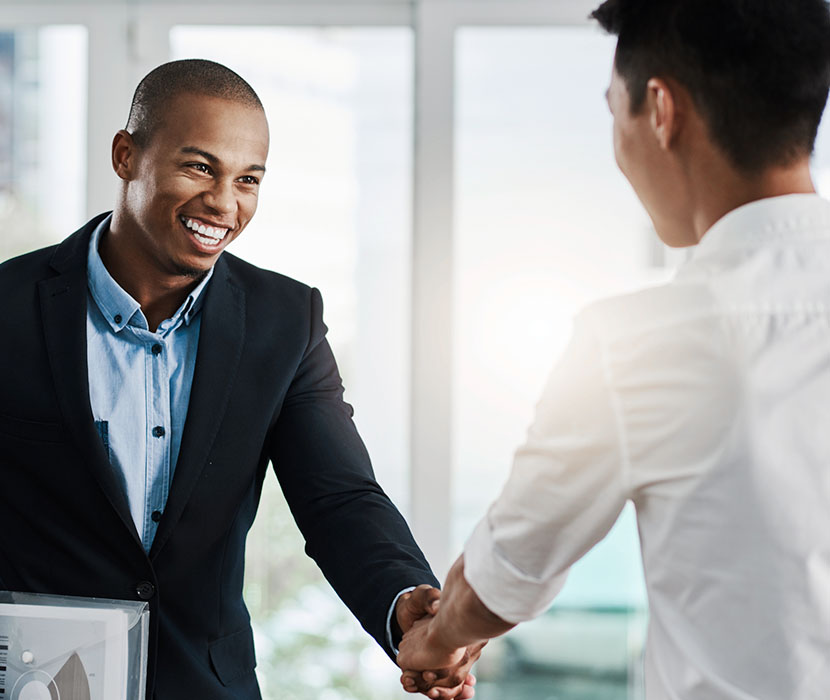  A Black male in a suit shaking hands with an asian male in an office