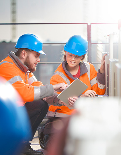 Co-workers with hard hats looking at a tablet.