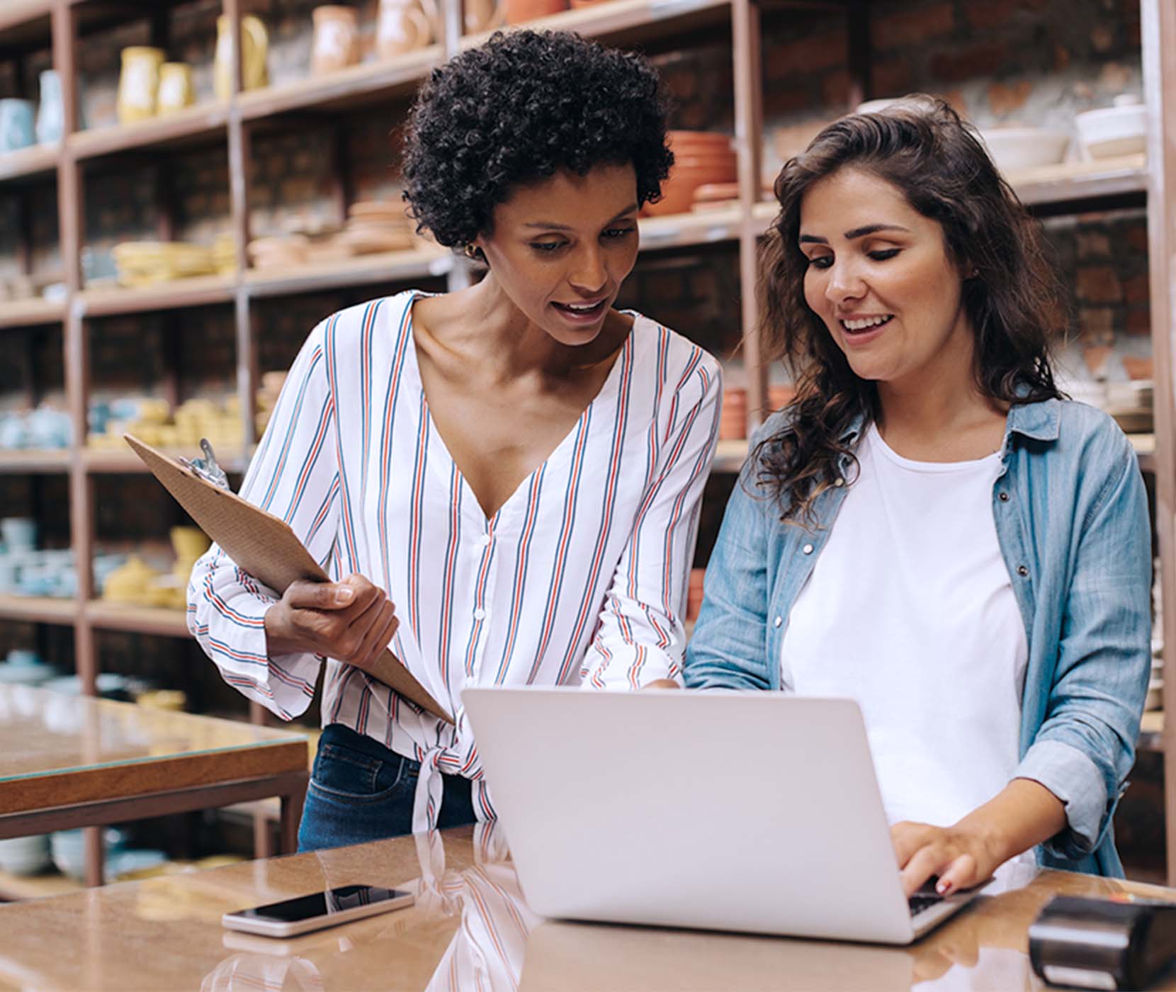 Two female co-workers in a retail store looking at the laptop