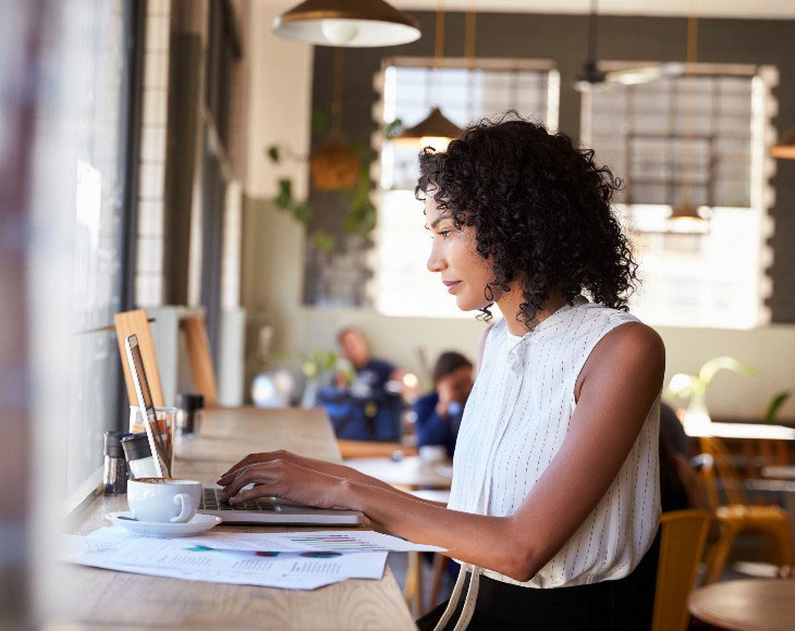 Businesswoman By Window Working On Laptop In Coffee Shop