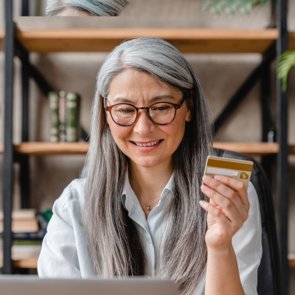 A woman holding a credit card looking at a laptop.